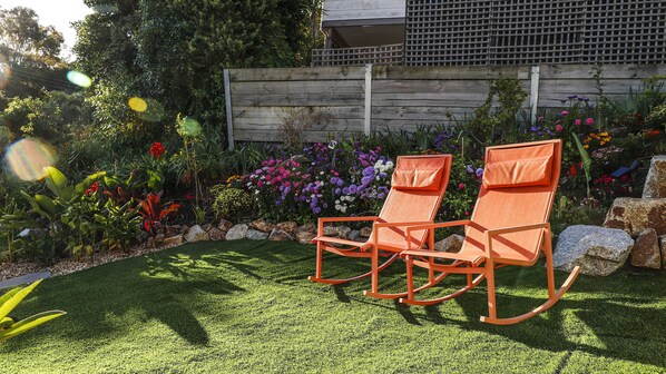 Two rocking chairs in a garden with a wooden fence and various colorful flowers.