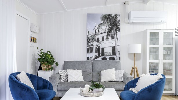 En stue med en grå sofa, to blå lænestole, et hvidt sofabord og et stort billede i ramme på væggen.