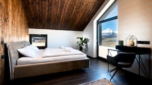 Un dormitorio moderno con techo de madera, una cama grande, un escritorio y vistas a la montaña.