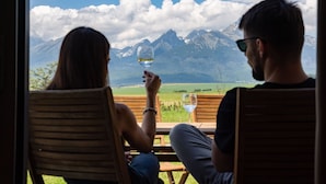 Dos personas sentadas en sillas de madera con vistas a una montaña.