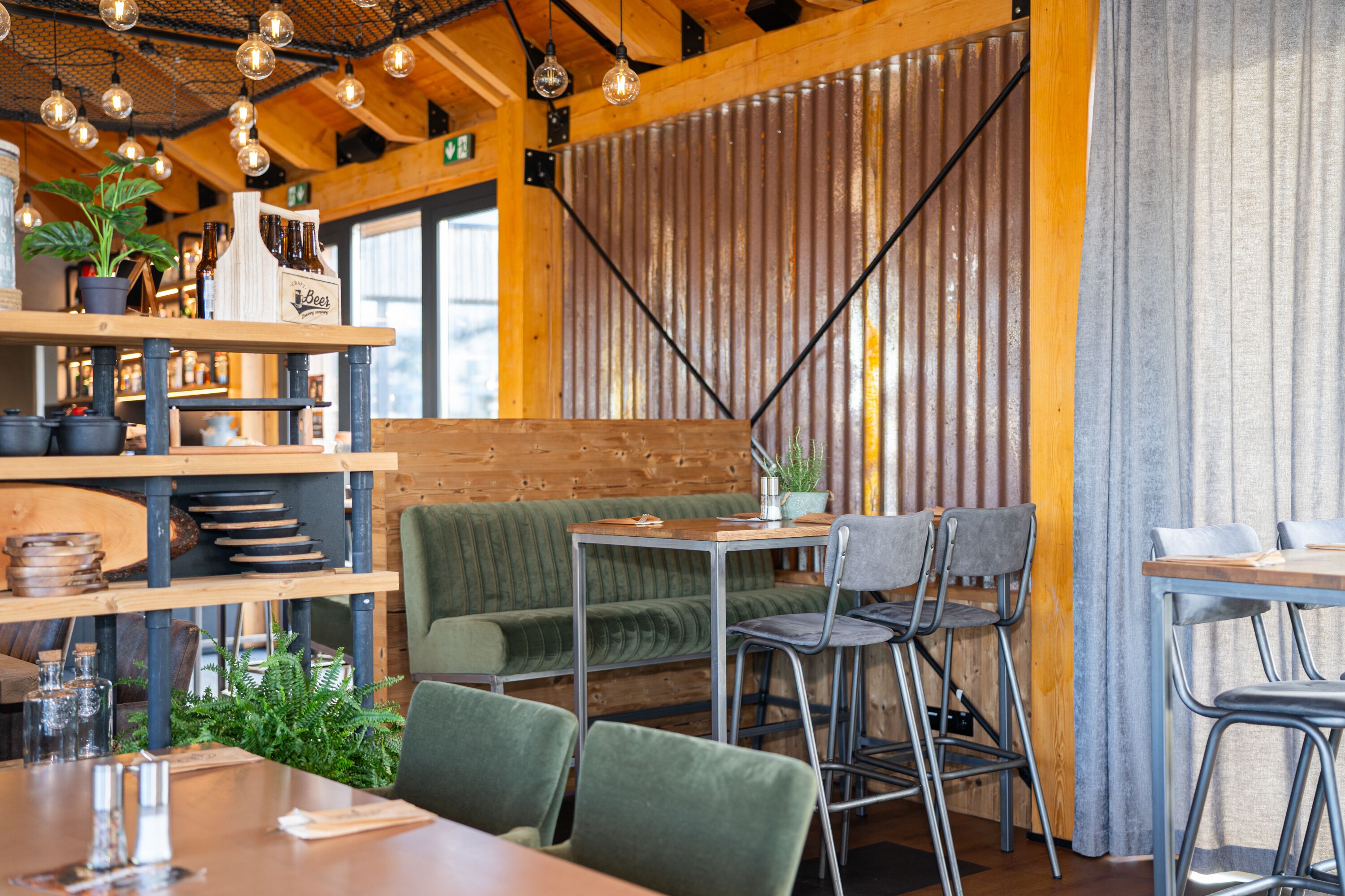 Ein Restaurant mit Holztischen und -stühlen, einer grün gepolsterten Bank und hängenden Leuchten.