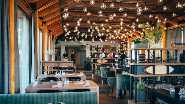 Un restaurante con mesas de madera, asientos tapizados en verde y lámparas colgantes esféricas.