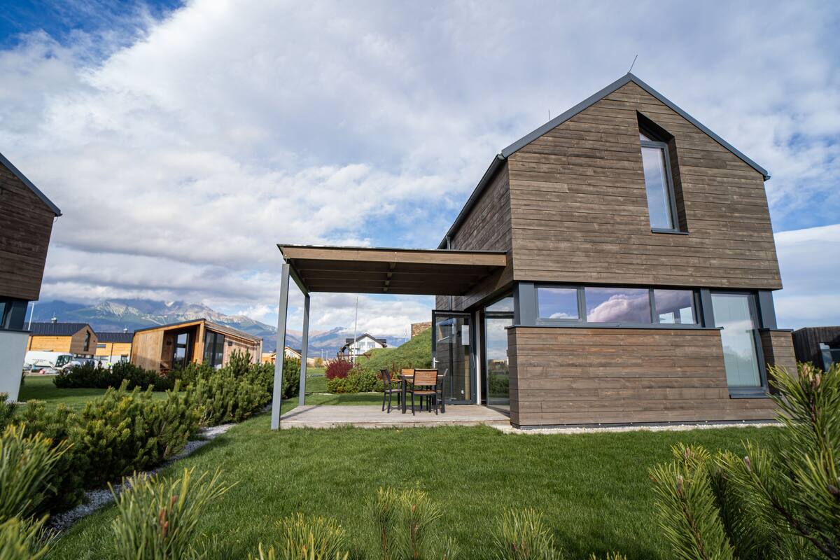 A modern two-story house with a covered patio and a view of mountains in the background.
