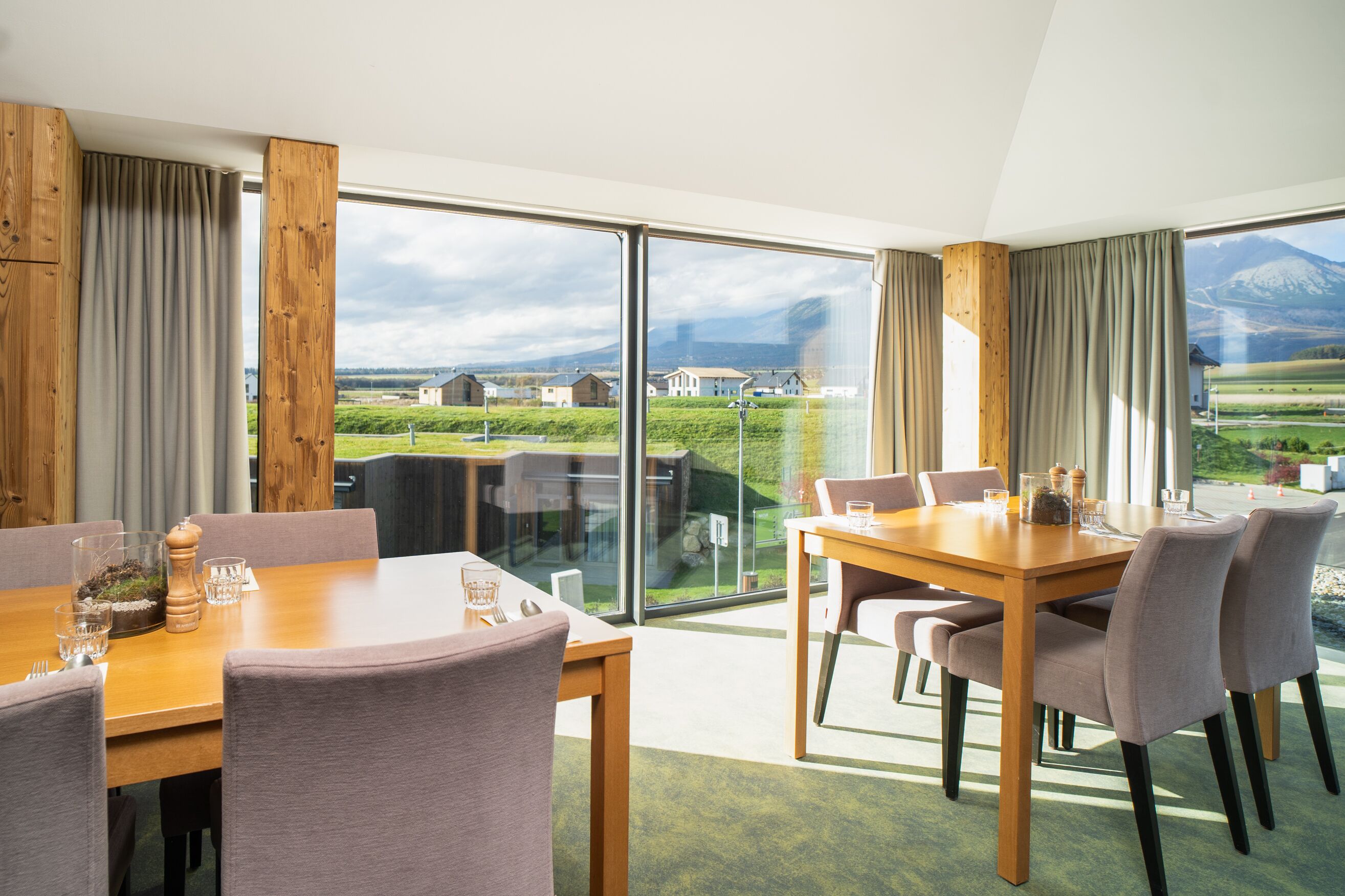 A dining area with a large table and chairs, a glass partition, and a view of a mountainous landscape through large windows.