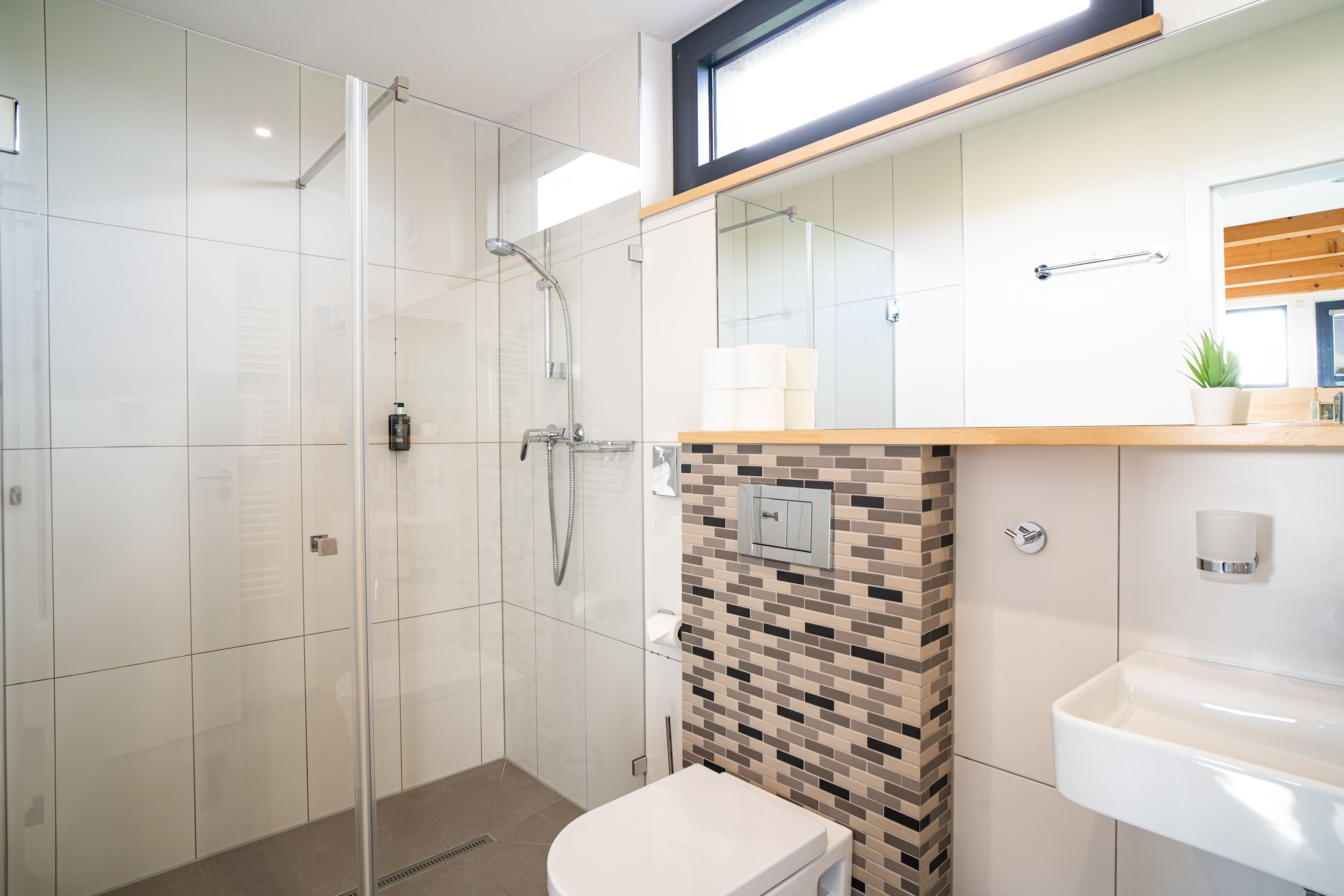 Een moderne badkamer met een glazen douchecabine, toilet, wastafel en een betegelde spatwand.