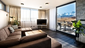 Una sala de estar moderna con un televisor de pantalla plana grande, un sofá y un comedor con vistas a las montañas.