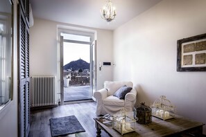 Une pièce avec une chaise blanche, une table avec des bougies, un radiateur et une vue sur le paysage urbain, visible à travers une porte vitrée.