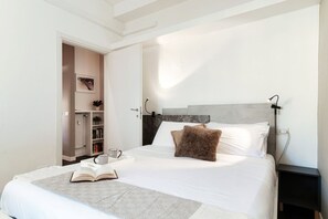 A bedroom with a bed, a nightstand, a bookshelf, and a door leading to another room.
