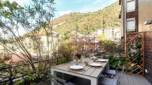 Uma área de refeições ao ar livre com uma mesa posta para quatro pessoas, rodeada por plantas e com vista para uma encosta.
