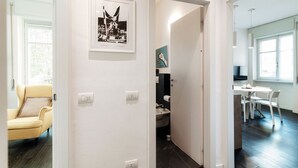 Um corredor com porta para um banheiro, uma área de jantar com mesa e cadeiras, e uma poltrona amarela.