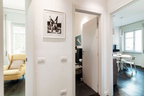 Un pasillo con una puerta que da a un baño, una zona de comedor con mesa y sillas, y un sillón amarillo.