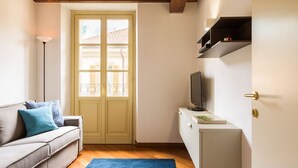 Una habitación con un sofá, un televisor sobre un mueble bajo, una puerta con ventanal y un estante.
