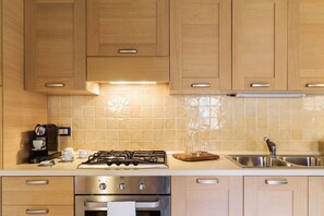 Een keuken met houten kastjes, een gasfornuis, een oven, een koffiezetapparaat en een spoelbak.