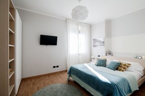 A bedroom with a bed, a TV, a window with curtains, a bedside table, and a wall-mounted picture.