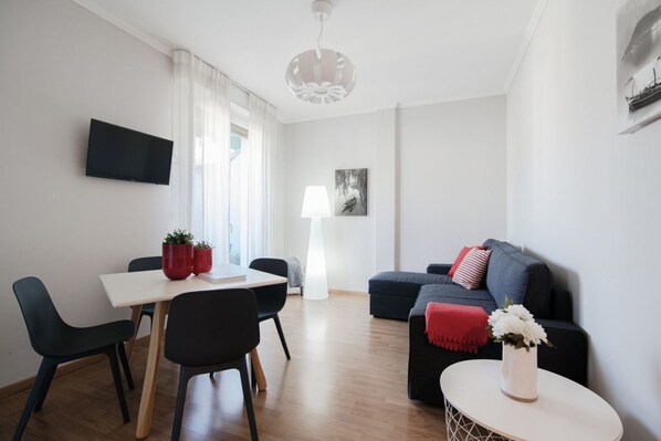 A modern living room with a dining area, a flat-screen TV, a lamp, and a sofa with a red throw blanket.
