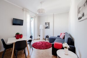 A modern living room with a sofa, a dining table with chairs, a TV mounted on the wall, and a red rug.