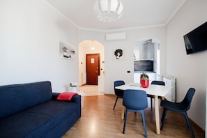 A modern living room with a sofa, dining table, chairs, and a TV mounted on the wall.