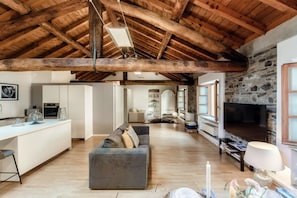 A spacious living area with a high wooden ceiling, a stone fireplace, and a modern kitchen in the background. - La Corte delle Rondini - My Home in Como (Como)