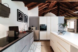 Una cocina moderna con estufa integrada, armarios blancos y techo de madera.