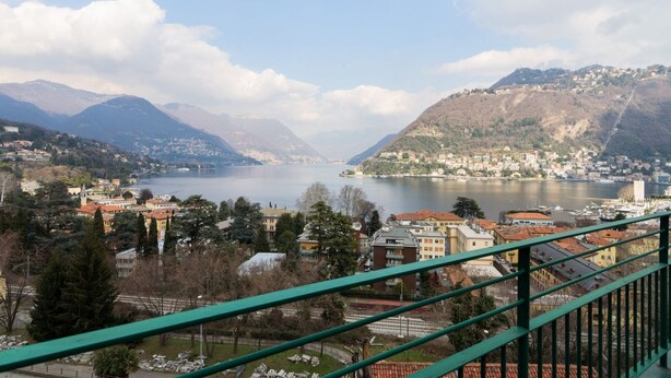 A panoramic view of a lakeside town with buildings, mountains, and a clear sky.