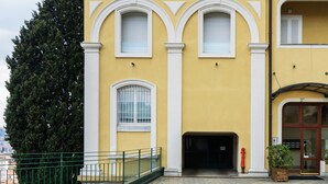 A yellow building with white trim, a green metal railing, and a large tree.