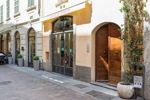 Un bâtiment doté d’une grande porte en bois, de fenêtres en arc de cercle et d’un pot de fleurs placé sur le trottoir.