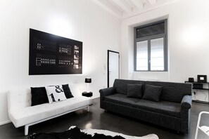 Ein modernes Wohnzimmer mit einem weißen Sofa, einem dunkelgrauen Sofa, einem schwarz-weißen Teppich und einem großen schwarz-weißen Kunstwerk an der Wand.