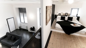 Ein modernes Zimmer mit einer Couch, einem Bett mit schwarzer Bettdecke und einem großen, abstrakten Gemälde an der Wand.