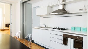A modern kitchen with white cabinets, stainless steel appliances, and a dining area with a black table and clear chairs. - Via Rusconi 10 - My Home In Como (Como)