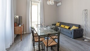Ett modernt vardagsrum med ett matbord i glas, en grå soffa och en golvlampa.
