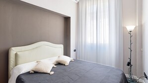 Ett hotellrum med en säng, en lampa och ett fönster med gardiner.
