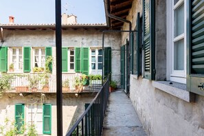 A narrow balcony with green shutters, a concrete floor, and a view of a building with similar shutters.