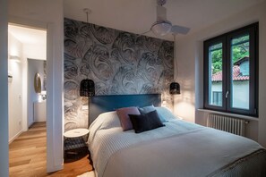 A bedroom with a patterned headboard, a bed with pillows, a round side table, and a window with a view.