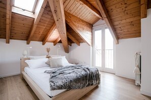 A bedroom with a sloped wooden ceiling, a bed with white bedding, a fluffy throw, and a window. - Modern Luxury Attic - My Home In Como (Como)
