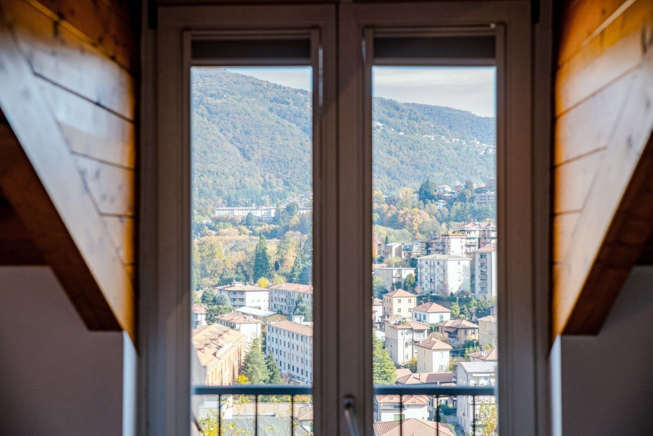Blick durch ein Fenster mit Holzbalkendecke auf eine Stadtlandschaft mit Gebäuden und Hügeln.