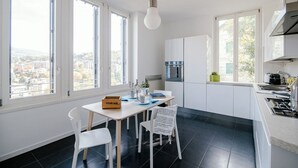 A modern kitchen with white cabinets, a dining table with chairs, and large windows offering a city view.