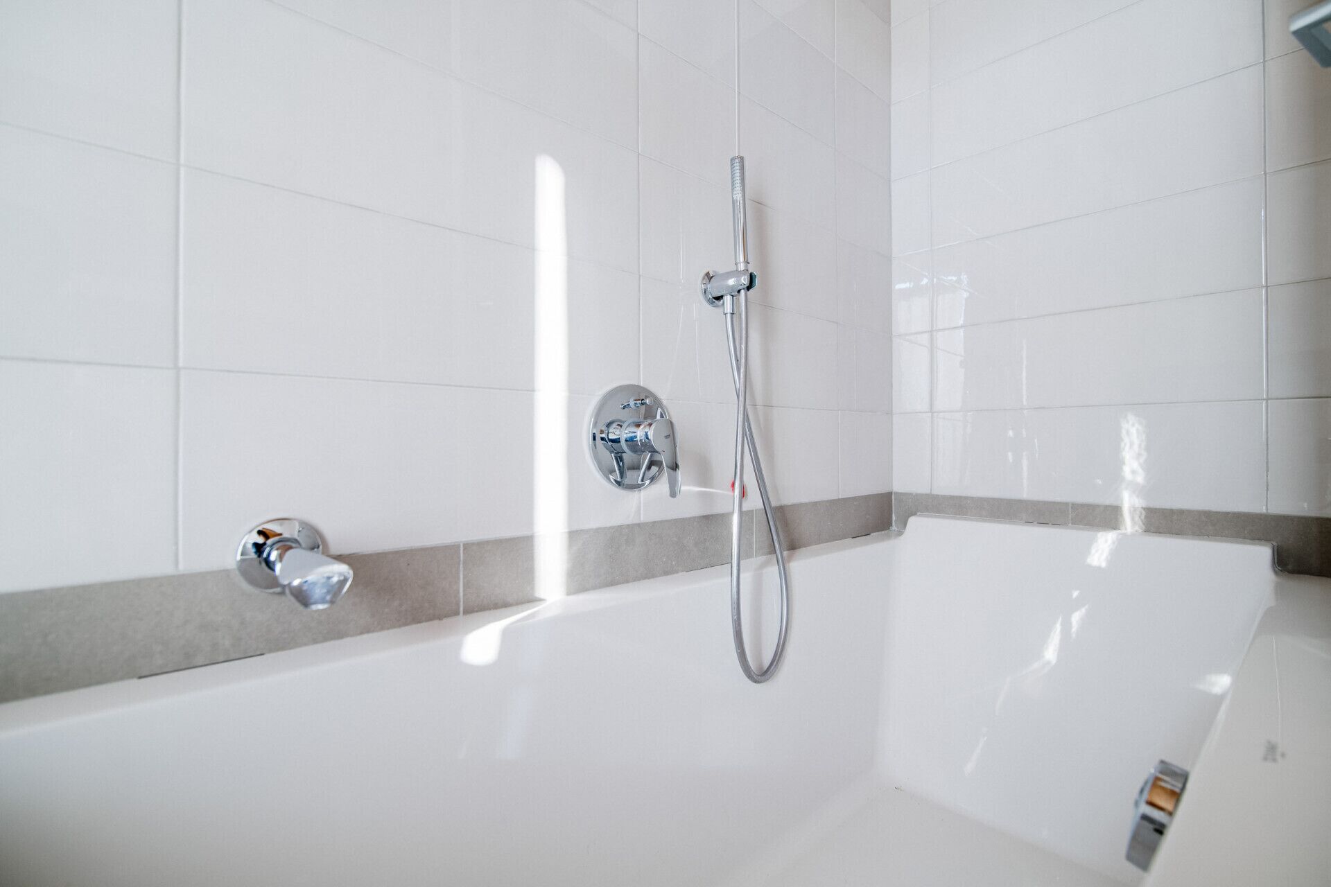 A modern bathroom with a white bathtub, a handheld showerhead, and a wall-mounted faucet.