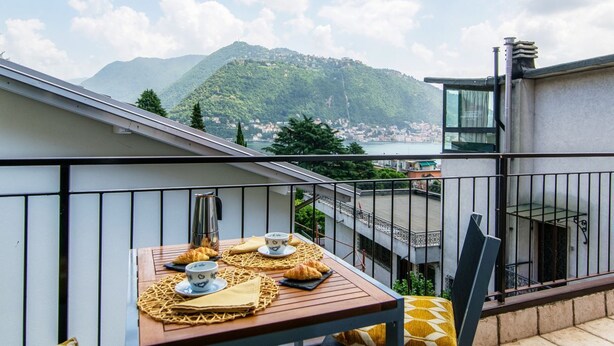 Un balcone con un tavolo apparecchiato per la colazione, con vista su un paesaggio montuoso.