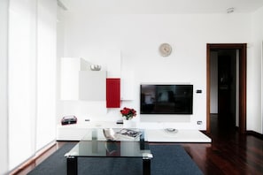 Ein modernes Wohnzimmer mit einem Glastisch, einem an der Wand befestigten Flachbildfernseher, einem roten Schrank und einer Uhr.