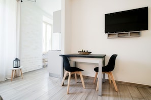 A modern dining area with a table, two chairs, a black TV mounted on the wall, and a small side table with a lantern. - S&O Apartment - My Home In Como (Como)