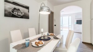 Un coin repas avec une table dressée pour deux personnes, une lampe, un tableau encadré au mur et une vue sur la pièce adjacente.