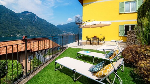Un bâtiment jaune doté d’un balcon donnant sur un lac et des montagnes.