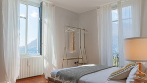 Ein Schlafzimmer mit Bett, Kleiderstange, einem Fenster mit Vorhängen und Blick auf einen Berg.