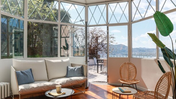 Ein sonnendurchflutetes Zimmer mit einer Couch, Sesseln und Meerblick.