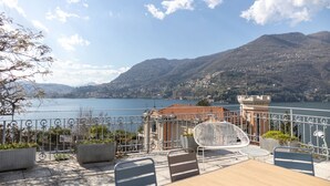 Eine Terrasse mit Sitzgelegenheit, Blick auf einen See und Berge im Hintergrund.