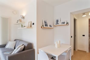 En moderne stue med en grå sofa, et hvidt bord og vægmonterede hylder med billeder.