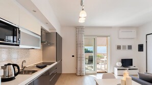 Una cocina moderna con microondas integrado, hervidor y pileta. Hay un comedor con mesa y velas. Un televisor está sobre un pedestal blanco.