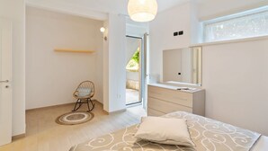 Un dormitorio con cama, mesita de noche, espejo, silla y puerta que da a un espacio exterior.