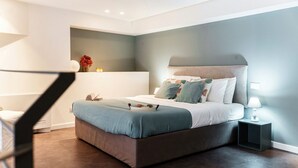 A modern bedroom with a large bed, bedside tables, and a built-in shelf with decorative items. - 06 Funicolare Visconti - My Home In Como (Como)