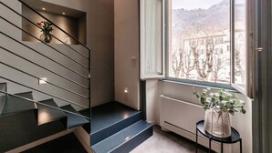 A modern staircase with a glass railing, a view of a cityscape through a large window, and a small table with a plant. - 06 Funicolare Visconti - My Home In Como (Como)